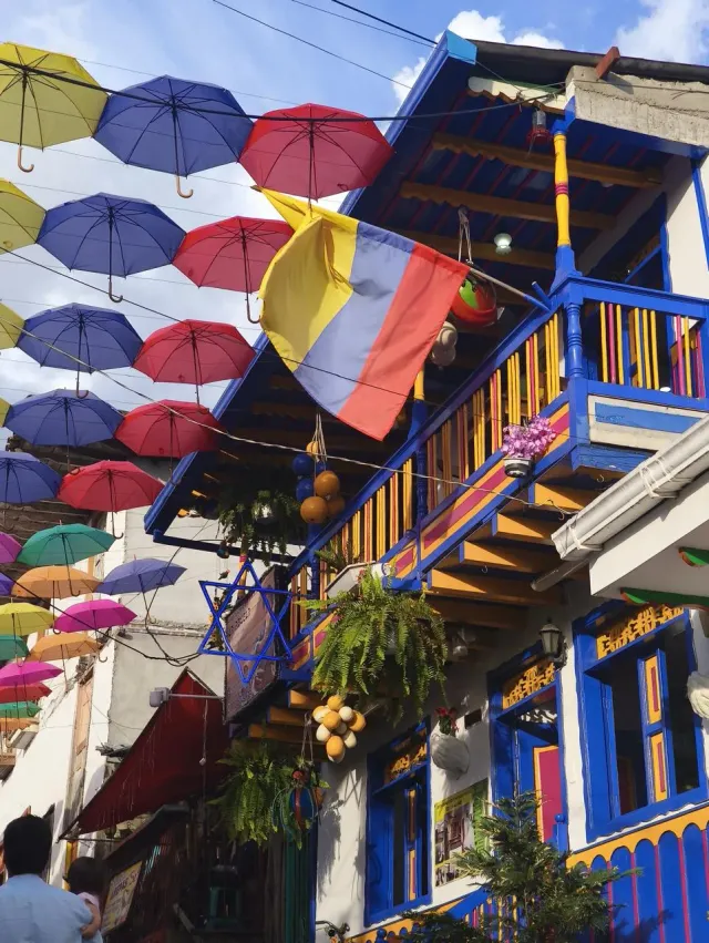 Calle de Salento decorada con sombrillas de colores y un balcón tradicional con la bandera de Colombia