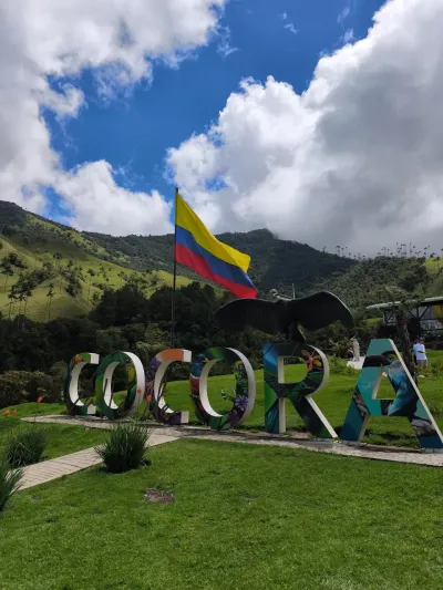 Letrero decorativo 'COCORA' con la bandera de Colombia y colinas verdes de fondo