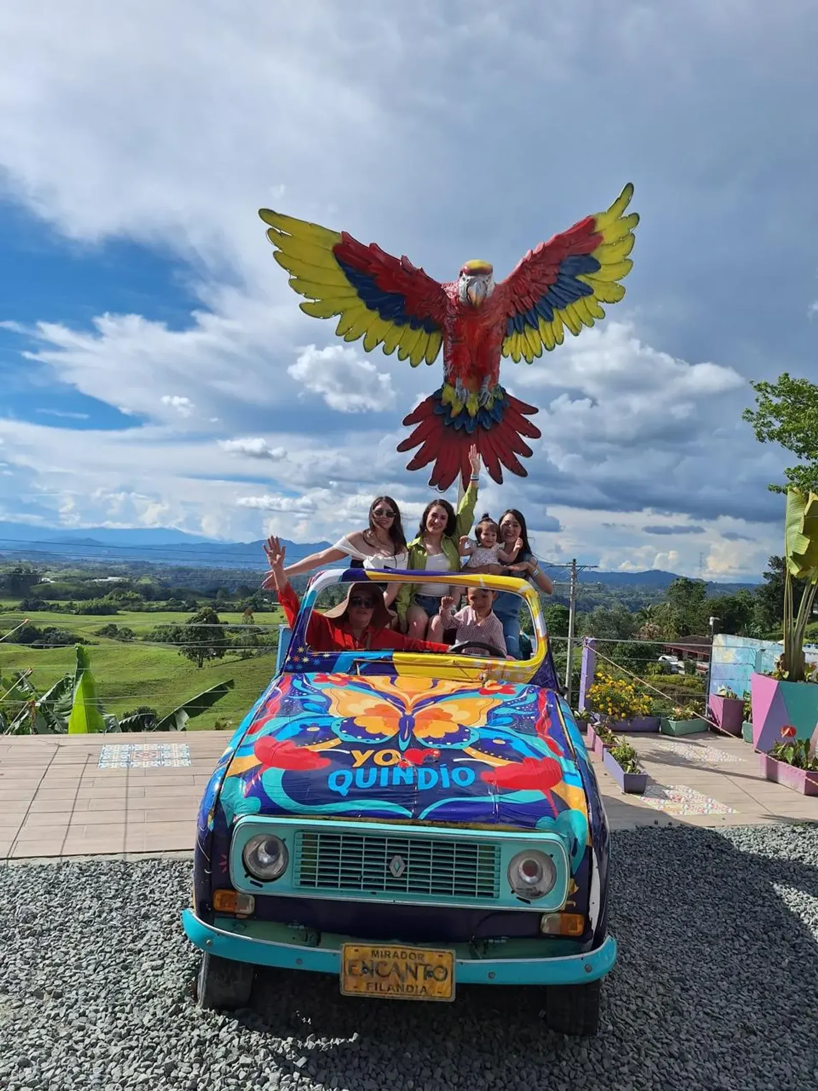 Grupo de turistas en un carro pintado bajo una escultura de guacamaya, en el mirador Encanto de Filandia