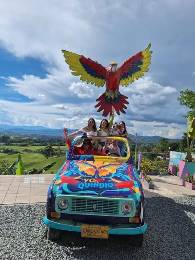 Grupo de turistas en un carro pintado bajo una escultura de guacamaya, en el mirador Encanto de Filandia