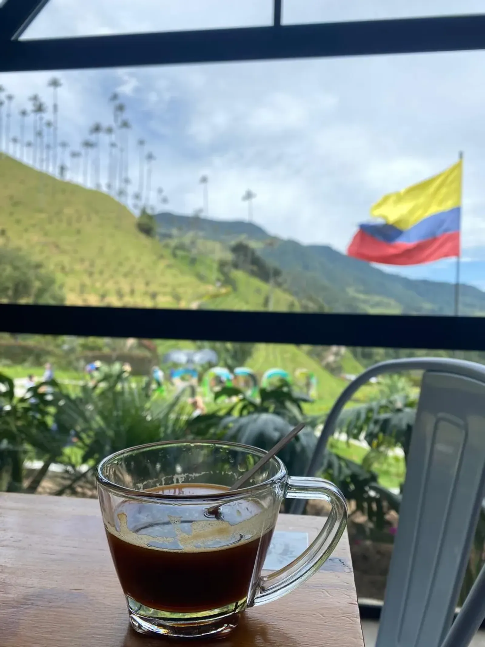 Taza de café colombiano con vista a colinas verdes y la bandera de Colombia de fondo