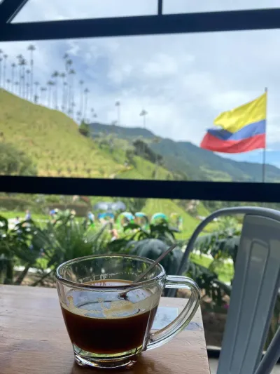 Taza de café colombiano con vista a colinas verdes y la bandera de Colombia de fondo