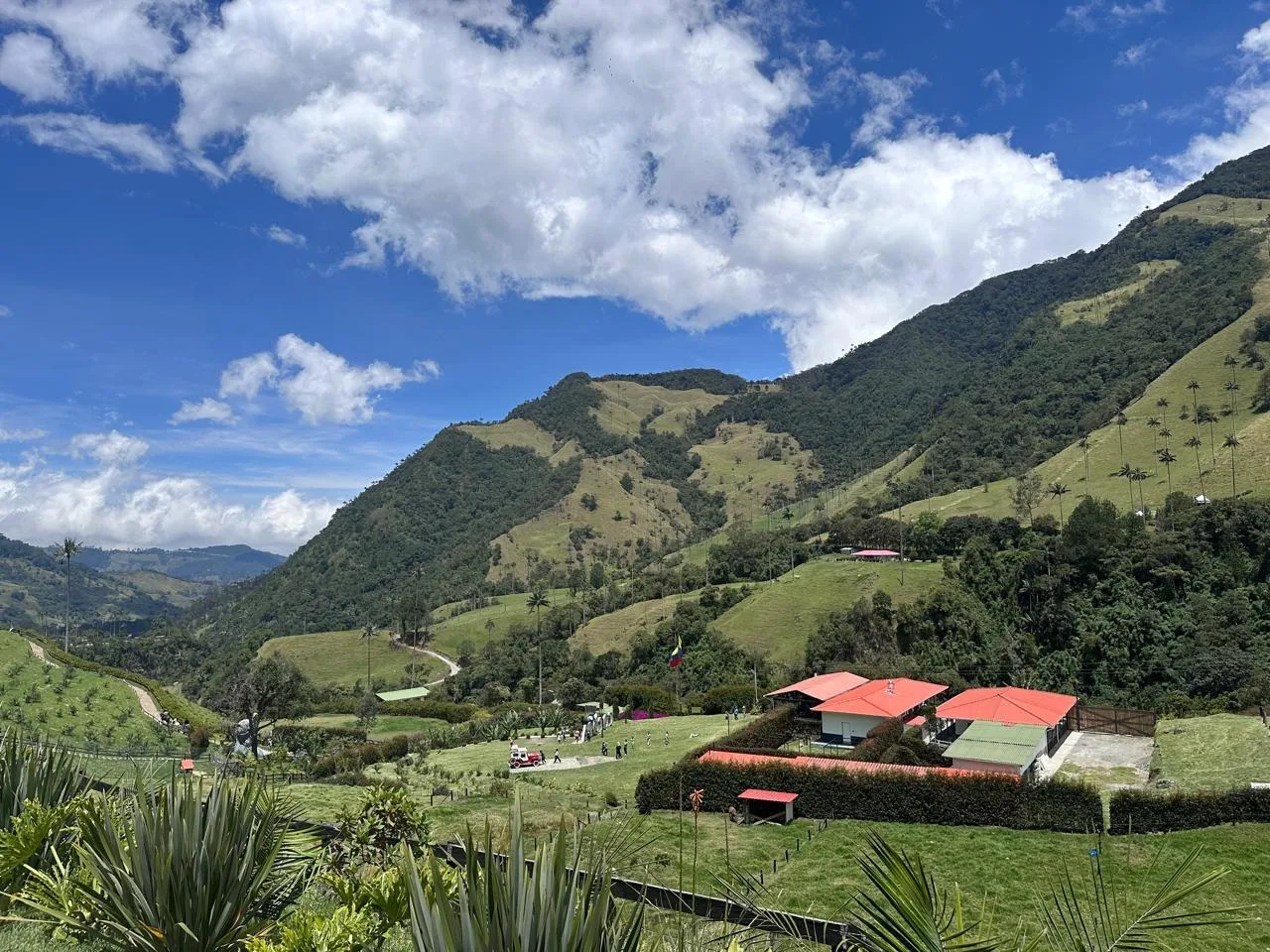 Montañas verdes bajo cielo azul con una finca de techos rojos
